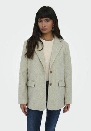 Blazer en laine gris clair avec deux boutons, col à revers et poches avant, porté sur un haut beige et un jean foncé. Texture lisse.