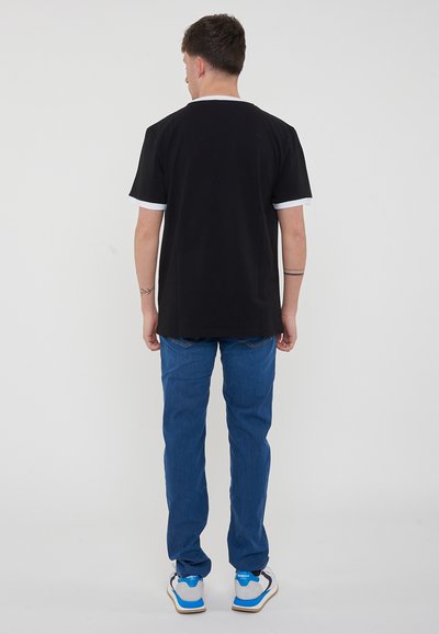 T-shirt in cotone nero con rifiniture bianche al colletto e alle maniche, abbinato a jeans in denim blu e sneakers bianche con accenti blu.