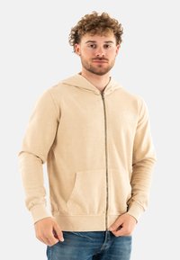 Felpa beige con zip realizzata in tessuto morbido, dotata di una tasca frontale, cappuccio con cordoncino e polsini a costine. Marchio discreto sul petto.