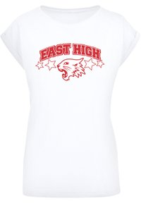 Valge T-särk üleskeeratud varrukatega, millel on punane graafika, mis ütleb "EAST HIGH" uriseva tiigri pea ja viie tähe kohal.