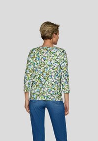 Damenoberteil in Grün, Blau und Gelb mit Sternmuster, drei Viertel Ärmeln; runder Ausschnitt; leichtes, glattes Material; kombiniert mit Jeans.