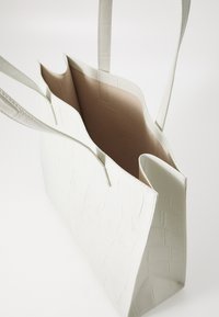 White faux leather tote bag with embossed crocodile texture, open top, soft beige interior, and two long handles for carrying.