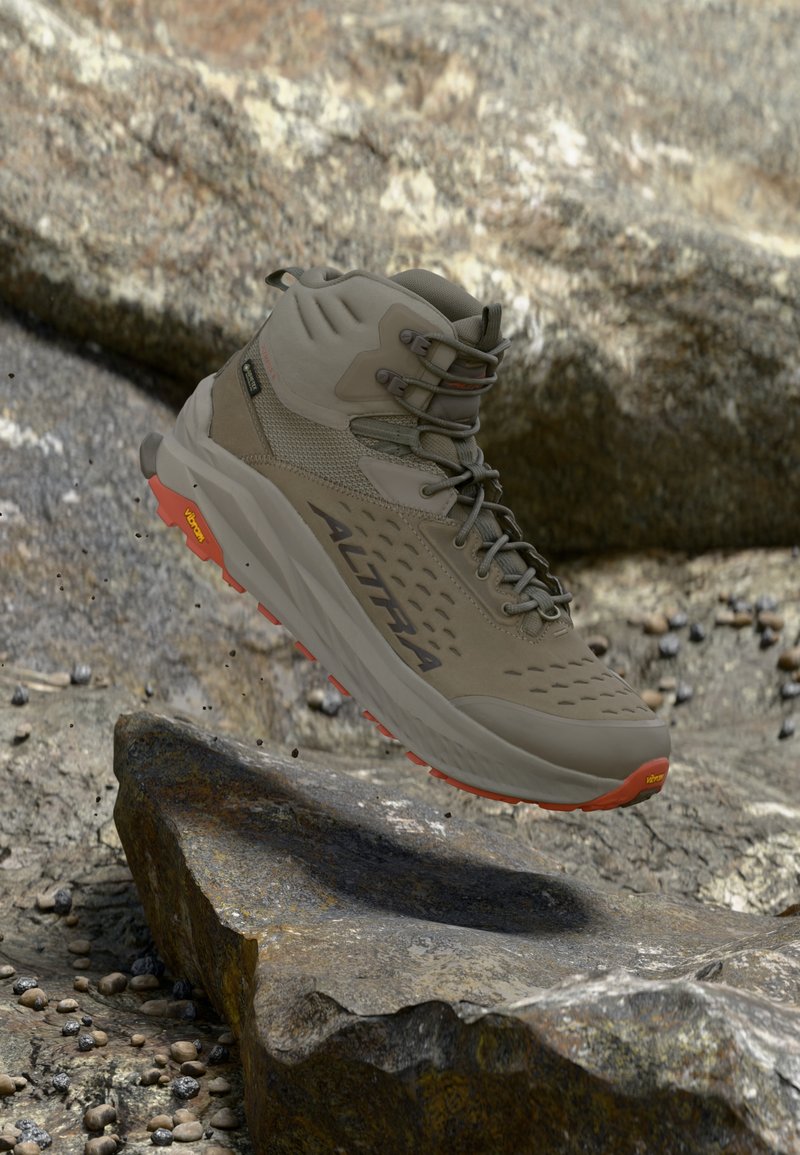 Μπότα πεζοπορίας με σόλα Vibram και λογότυπο Altra, στον αέρα πάνω από βραχώδες έδαφος με μικρές σκορπισμένες πέτρες και μεγάλο πέτρινο φόντο.