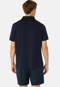 Navyblauwe polo met klassieke kraag, korte mouwen en een soepele textuur. Heeft een stijlvolle achterste schoudernaad. Gecombineerd met navy shorts.