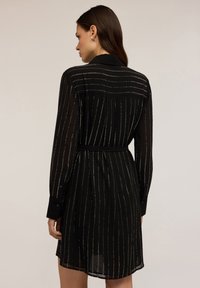 Abito nero a maniche lunghe con strisce metalliche verticali, vita con cintura e texture trasparente. Colletto discreto e polsini con bottoni.