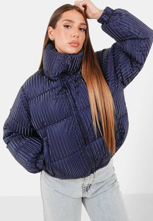 Marinblå puffjacka med hög krage, quiltad design och framträdande horisontella ränder. Har en framfickdragkedja och sidofickor.