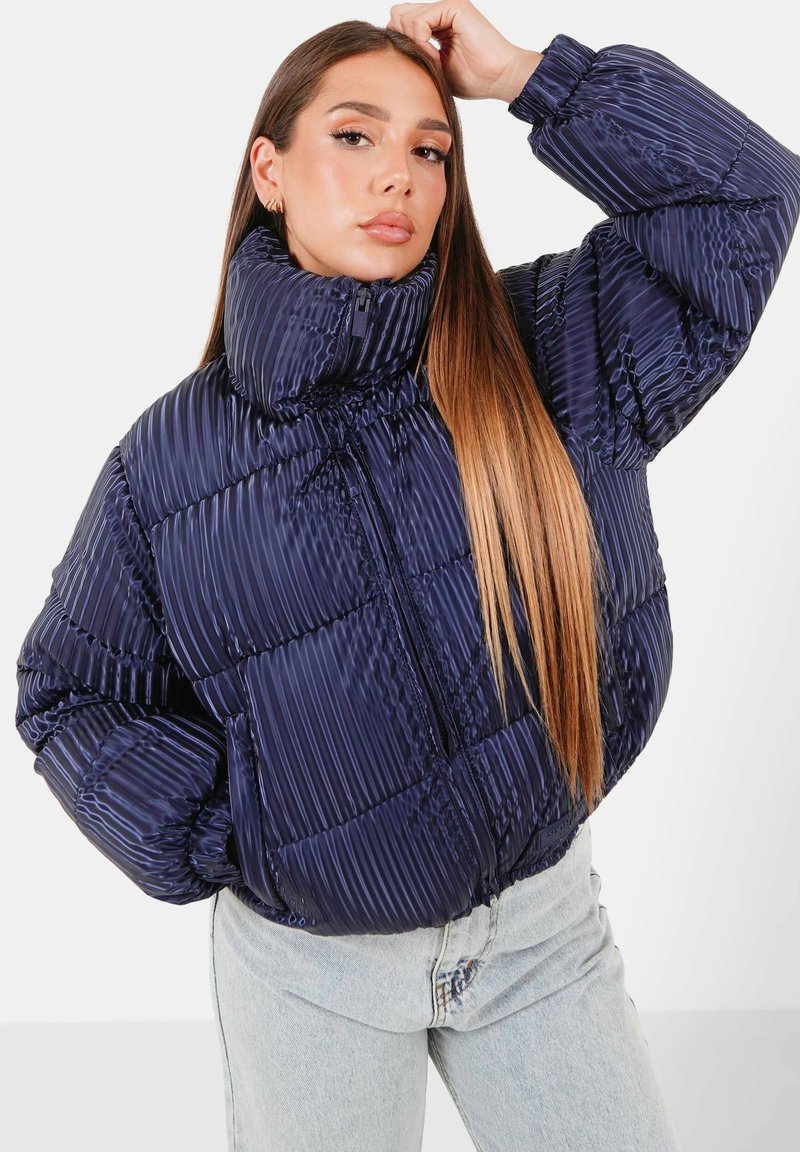 Giacca trapuntata navy con colletto alto, design a quadri e righe orizzontali prominenti. Presenta una zip frontale e tasche laterali.