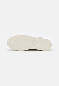 Suola delle scarpe in gomma avorio con motivo a spina di pesce, con logo del marchio. Parte superiore liscia marrone, forma arrotondata e senza elementi hardware visibili.