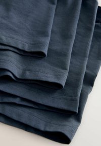 Fyra vikta mörkblå T-tröjor av slät tyg med korta ärmar och rena kanter, som visar subtila sömnadsdetaljer.