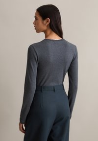 Szary prążkowany top z długim rękawem, zestawiony z wysokim stanem i ciemnoturkusowymi spodniami; posiada zaokrąglony dekolt i gładką fakturę.