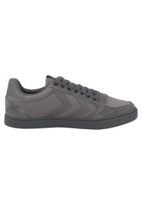 Sneaker atletica grigia con tessuto sintetico e dettagli in camoscio. Presenta una punta tonda, suola piatta e una chiusura con lacci decorativa.