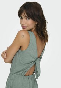 Lichtgroen mouwloos jurkje met een gestrikt ontwerp aan de achterkant, gestructureerde stof en een open rug. Heeft een ronde halslijn en een geplooide taille.