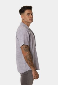 Camisa de botón de manga corta en tejido gris claro con un patrón texturizado, que presenta un corte relajado y un diseño de cuello clásico.