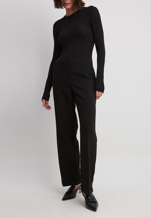 Zwarte longsleeve top met een aansluitende silhoutte, gecombineerd met hoge, wijde zwarte broek. Glad textuur en minimale ontwerpelementen.