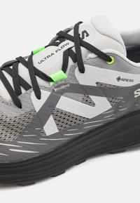 Pantof gray sportiv cu un superior din plasă, șireturi negre, accente verzi și o talpă din cauciuc texturată cu un model de profil distinct.