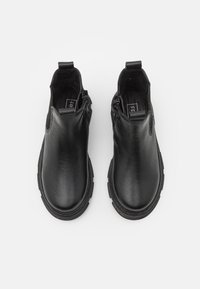 Botas negras de cuero hasta el tobillo con una textura suave, paneles laterales elásticos y una suela texturizada ligeramente elevada. Detalle de cierre de cremallera.