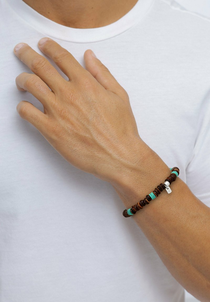 Brun pärlarmband med turkosa detaljer och en silversmycke. Träpärlor i varierande storlekar ger textur och visuell intresse.