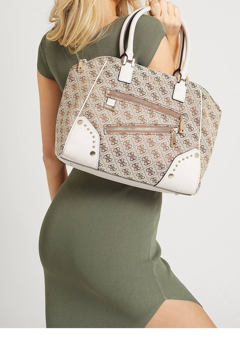Femme en robe verte ajustée tient un sac à main beige à motifs avec des poignées blanches et des poches zippées sur l’épaule.