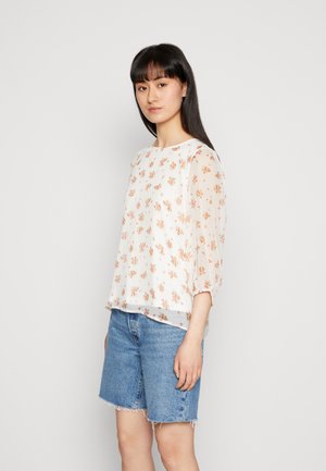 Blusa floral em tecido leve e transparente branco com flores em pêssego e verde. Apresenta mangas 3/4 e um corte relaxado. Combinada com calções de ganga.