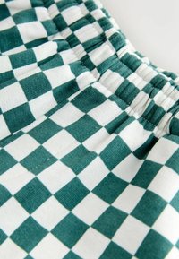 Zeleno-biele kockované tkanivo s elastickým pásom. Mäkká textúra s vzorom striedajúcich sa štvorcov. Navrhnuté pre pohodlie.
