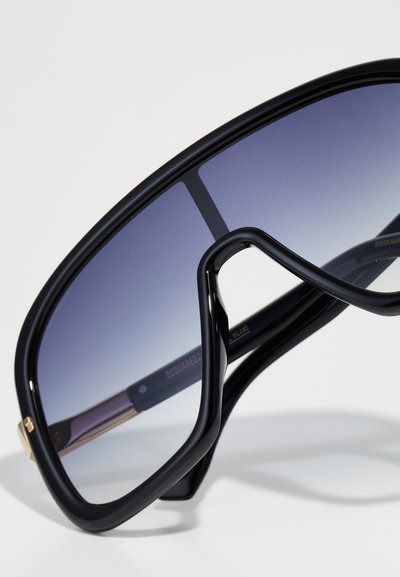 Black oversized sunglasses with gradient gray lenses, bold curved frame, glossy finish, and gold accents on the temple.
