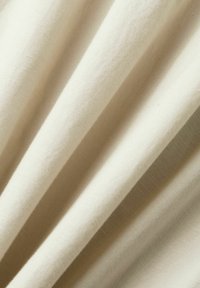 Tela de crema clara con una textura suave, que muestra hilos finos y un sutil brillo, dispuesta en suaves pliegues.