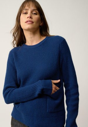 Pull en tricot bleu avec texture côtelée, manches longues, col rond et une poche à l'avant. Le tissu semble chaud et décontracté.