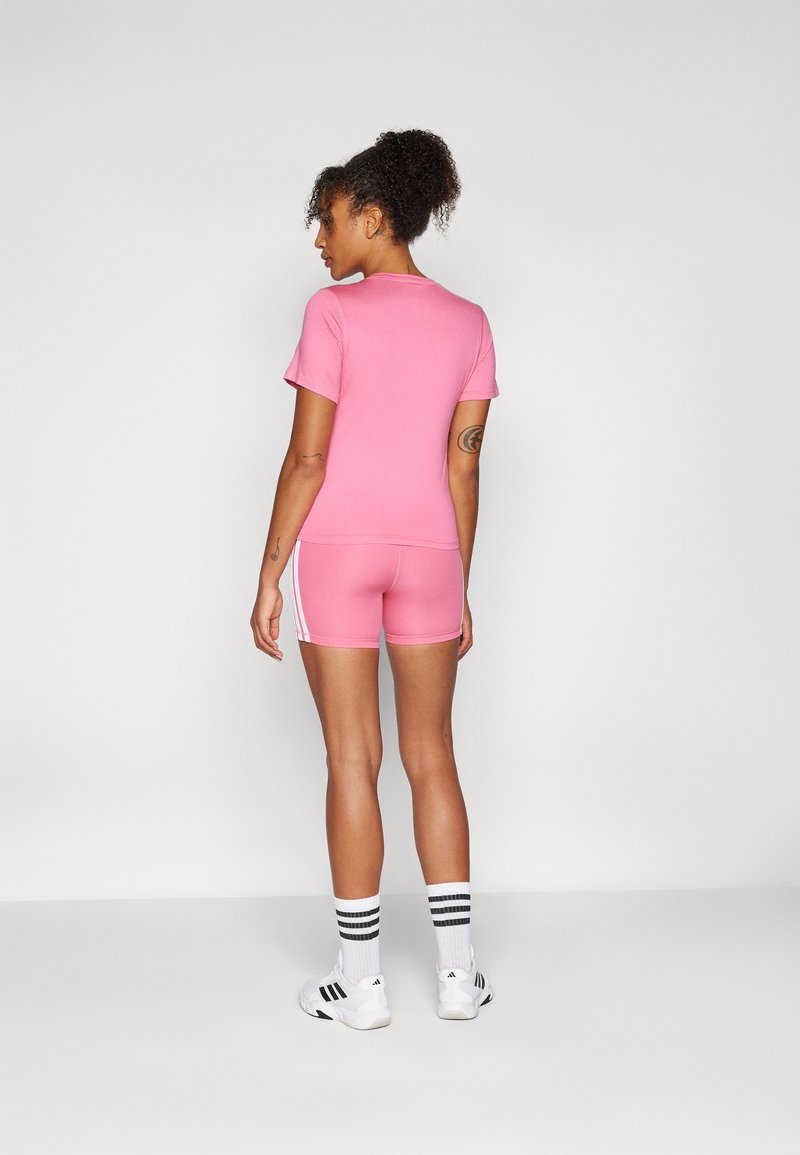 Ensemble de haut et de shorts de sport rose. Tissu lisse, design ajusté, manches courtes et rayures blanches contrastantes sur les côtés. Porté avec des baskets blanches et des chaussettes rayées.