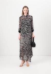 Durchsichtiges Leopardenmuster-Kleid mit Kragen, langen Ärmeln und schwarzen Bündchen. Faltensaum. Trägt dazu Riemchensandalen und hält eine schwarze Handtasche.