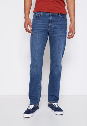 Blue denim jeans with a straight fit, five-pocket design, light fading, and subtle stitching details, paired with navy sneakers.