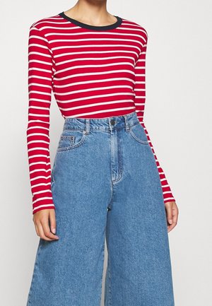 Maglietta a maniche lunghe a righe rosse e bianche con colletto girocollo blu navy, abbinata a jeans in denim a vita alta e gamba larga di colore blu chiaro.