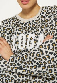 Felpa con stampa leopardata in grigio chiaro con dettagli neri e dorati. Presenta un collo rotondo e la parola "YOGA" in lettere bianche bold.
