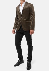Brun fløjl blazer med notch lapels, to knapper og sidelommer, parret med sorte slim-fit bukser og sorte lædersko.