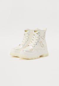 White ankle boots with a shiny, iridescent finish, featuring butterfly cut-out designs, white laces, and thick rubber soles.