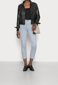 Chaqueta de cuero negra corta sobre una blusa negra de canalé, jeans skinny azul claro y mocasines negros. Bolso gris con detalles en negro.