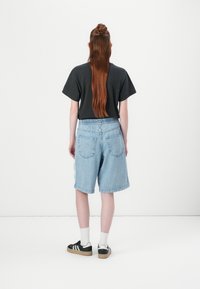 Bermuda in denim di colore blu chiaro con vita elasticizzata, due tasche posteriori e una vestibilità ampia. Maglietta nera a maniche corte e sneakers nere con dettagli bianchi.