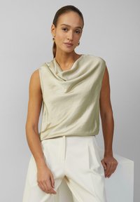 Hellbeige satin ärmelloses Oberteil mit drapiertem Ausschnitt. Kombiniert mit weißen, hoch taillierten Hosen mit vorderen Falten.