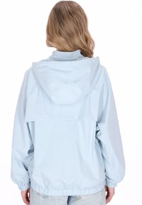 Vaaleansininen vedenpitävä takki hupulla, joustavilla resoreilla hihoissa ja kiristysnyörillä helmassa. Takana on läppätasku ja takissa on sileä pinta.