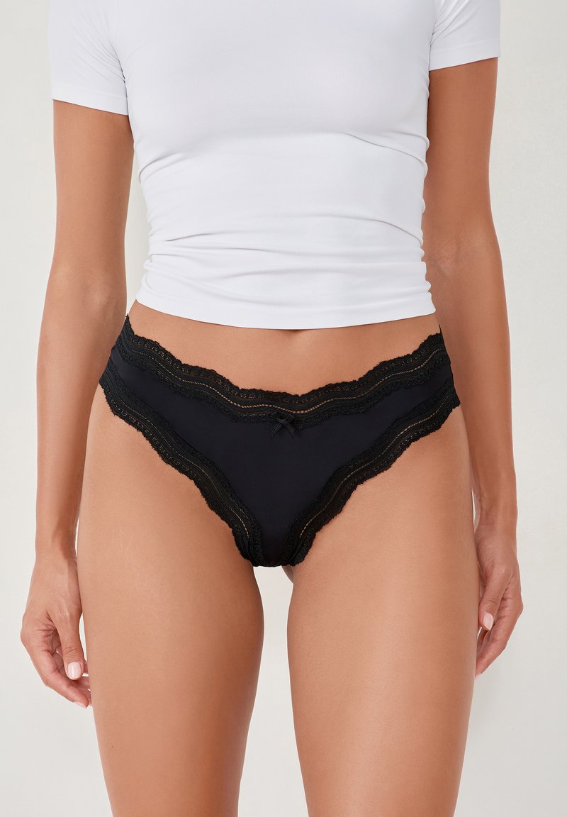 Schwarze Panties mit Spitze, aus einem glatten, weichen Stoff, mit gewelltem Saum und einer kleinen dekorativen Schleife in der Mitte vorne.