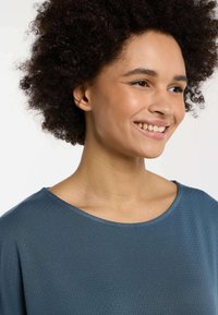 Top texture turchese con ampia scollatura rotonda. Il tessuto presenta un motivo sottile e le maniche sono leggermente morbide.