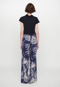 Black short-sleeve top paired with wide-leg navy trousers featuring a white palm leaf print. Smooth texture and relaxed fit.