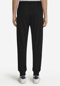 Czarne dresowe spodnie z wygodnym elastycznym pasem, zwężające się przy kostkach, zestawione z białymi sneakersami z niebieskimi akcentami.