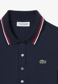 Polo shirt slim fit Lacoste di colore blu navy con colletto a righe rosse, bianche e blu navy e logo coccodrillo verde sul petto sinistro.