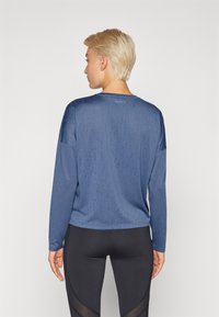 Camicia a maniche lunghe di colore blu profondo, realizzata in tessuto traspirante, con scollatura rotonda e spalle scese, dotata di una leggera lucentezza.