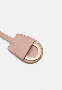 Portachiavi in pelle color rosa tenue, caratterizzato da un anello metallico rotondo dorato con la scritta "ANNA FIELD" incisa. Texture liscia, forma rettangolare con bordi cuciti.