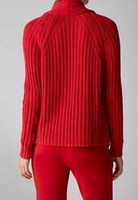 Pull rouge à côtes avec un col montant, doté de manches longues et d'une coupe ajustée, associé à un pantalon rouge assorti.