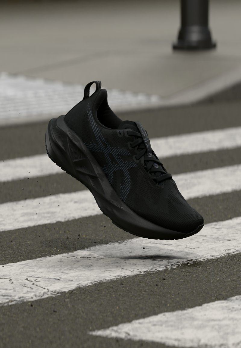 Μαύρο αθλητικό παπούτσι με υφασμάτινο επάνω μέρος, διακριτικό λογότυπο και επενδυμένη σόλα, αιωρούμενο πάνω από μια διαδρομή πεζής με ρίγες.