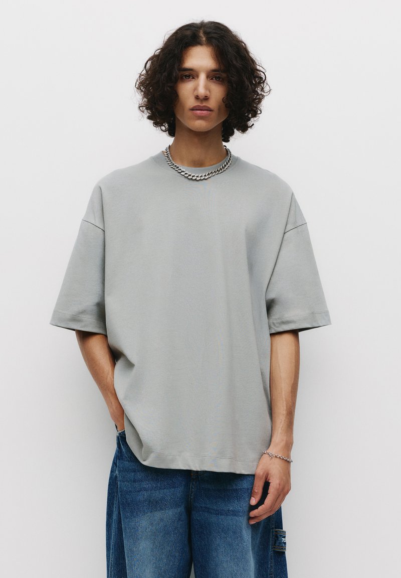 T-shirt grigio oversize, maniche corte, texture liscia, scollatura tonda, abbinato a jeans in denim blu larghi, con tasca laterale.