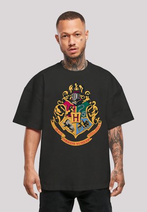 Black oversized t-shirt featuring a colorful emblem with a shield design and text. Notable graphics include various animal motifs and crowns.