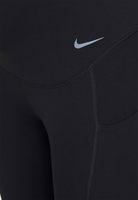 Czarne legginsy sportowe o gładkiej fakturze, z boczną kieszenią i małym, jasnoniebieskim logo Nike nad biodrem.